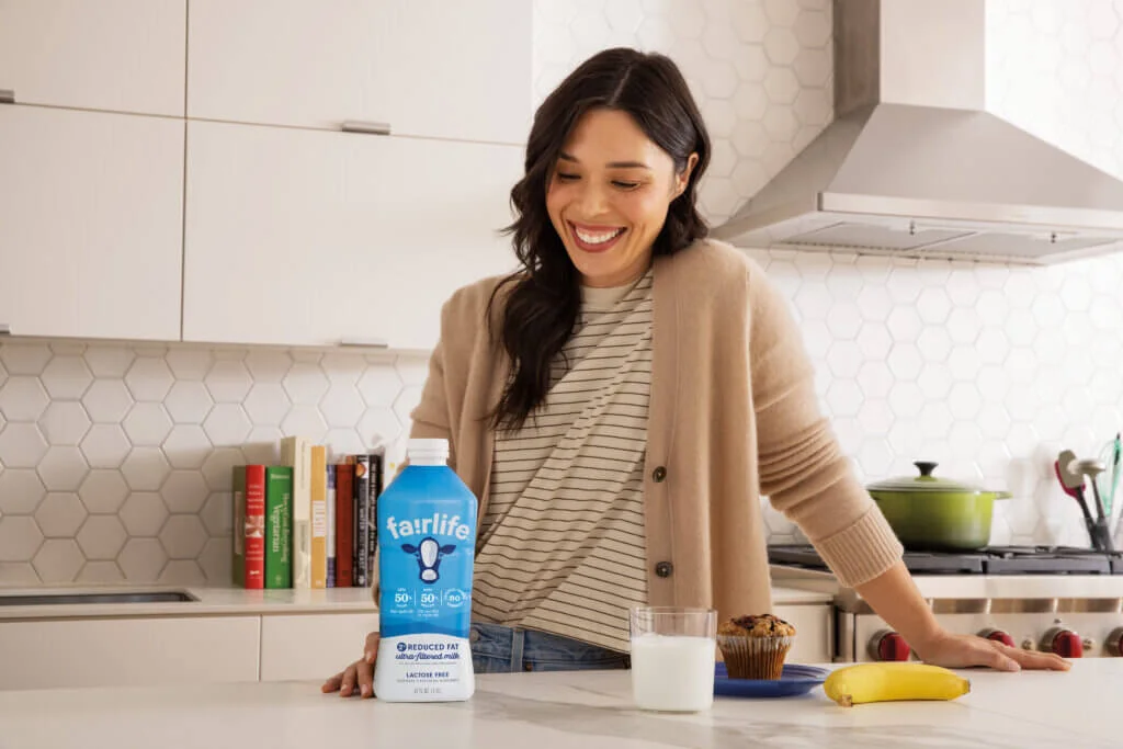 A woman enjoys a glass of fairlife ultra-filtered milk in a kitchen.